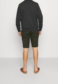 Sudadera negra, pantalones cortos verde oliva y sandalias marrones. El material parece suave; el ajuste es relajado. Los pantalones cortos terminan justo por encima de las rodillas.