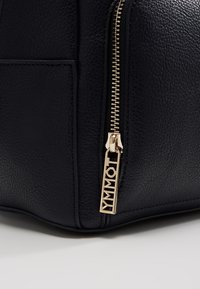 Gros plan d'un coin de sac en cuir noir texturé avec une fermeture éclair dorée et un curseur de fermeture éclair doré de marque.
