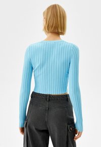 Ljusblå ribbad långärmad crop top med rund halsringning, tillsammans med högmidjade mörkgrå byxor med sidfickor.