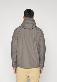 Γκρι αδιάβροχο μπουφάν με κουκούλα, με λείο ύφασμα και μινιμαλιστικό σχέδιο. Ορατές ραφές κατά μήκος των ραφών.