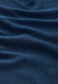 Marineblauwe textuurstof met verticale ribbelpatronen en een zachte, gladde oppervlakte, gedrapeerd om plooien en het spel van licht op het materiaal te tonen.