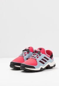 Urheilukengät, joissa on hengittävä punainen verkko-osa, siniset aksentit, musta pohja ja säädettävä nauhajärjestelmä. Sivussa on kolme mustaa raitaa.