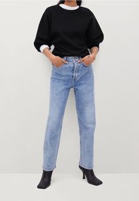 Černá oversized mikina, bílý vnitřní límec, světle modré džíny se zvýšeným pasem, rovné nohavice, kombinované s černými kotníkovými botami.