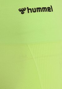 Ljust gröna träningsleggings i ribbat tyg, med en svart "hummel"-logotyp vid midjan och en slät textur.