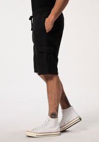 Schwarze Cargo-Shorts in lockerer Passform, mit Seitentaschen und einem elastischen Bund. Das Material ist glatt mit einer matten Oberfläche.