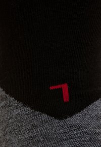 Calze testurizzate nere e grigie con un dettaglio in rosso a punto di contrasto che rappresenta il numero sette vicino alla parte superiore. Design a costine per una maggiore aderenza.