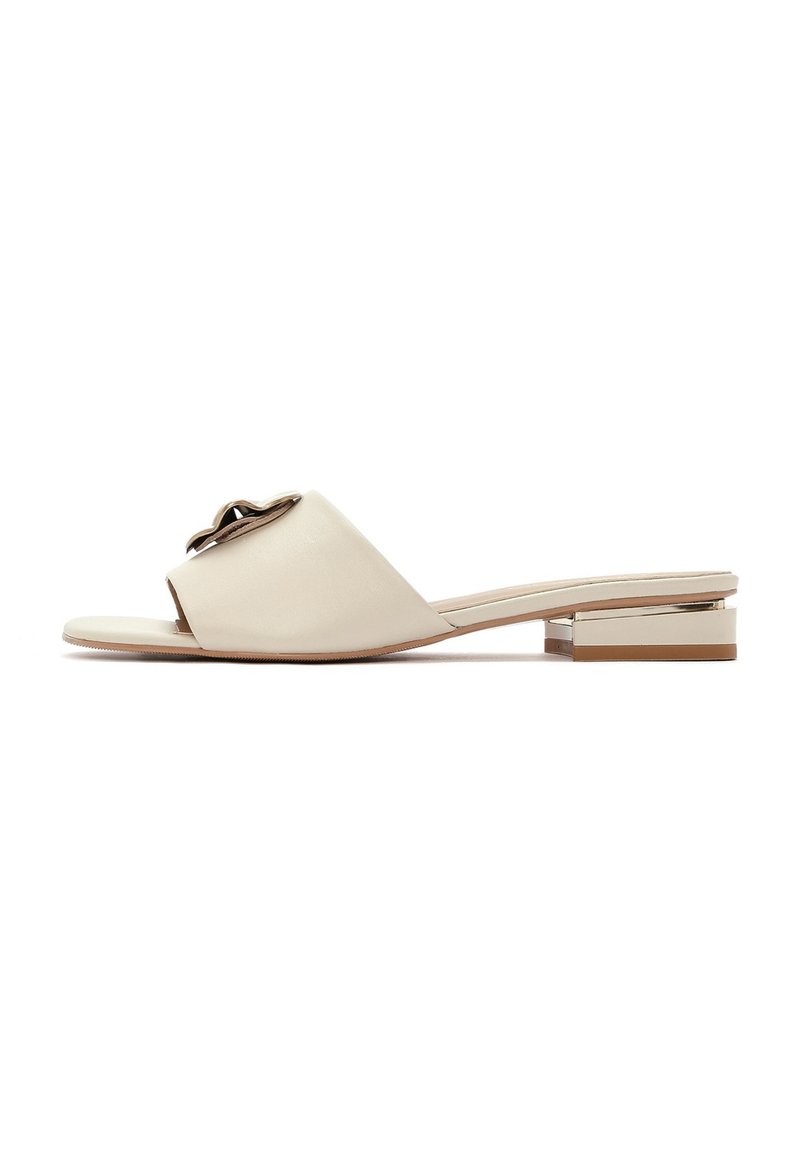 Beige leren slipper sandaal met een open teen, voorzien van een metallische accent en een lage vierkante hak met een goudkleurig detail.