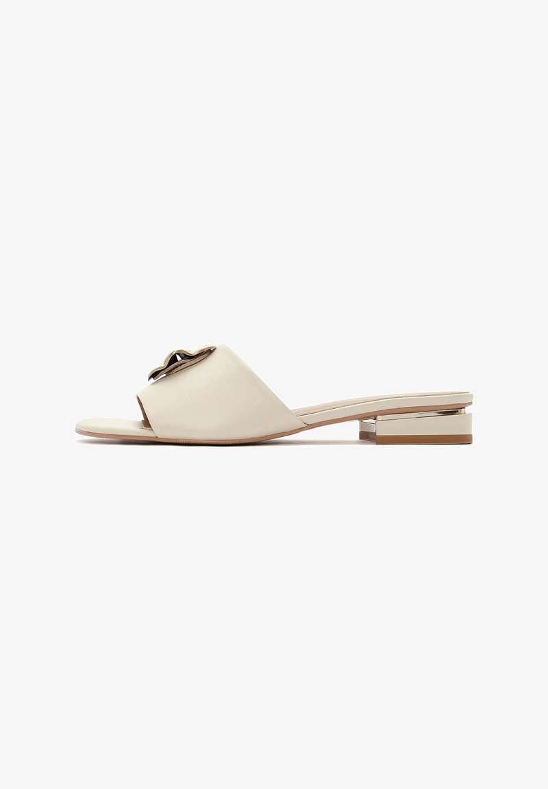 Sandale à glissière en cuir beige avec un bout ouvert, présentant un accent métallique et un petit talon carré avec un détail en ton or.