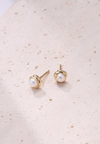 Gouden studoorbellen met een ronde witte parel in een ingewikkeld gevlochten ontwerp, met een gepolijste afwerking en een gladde textuur.