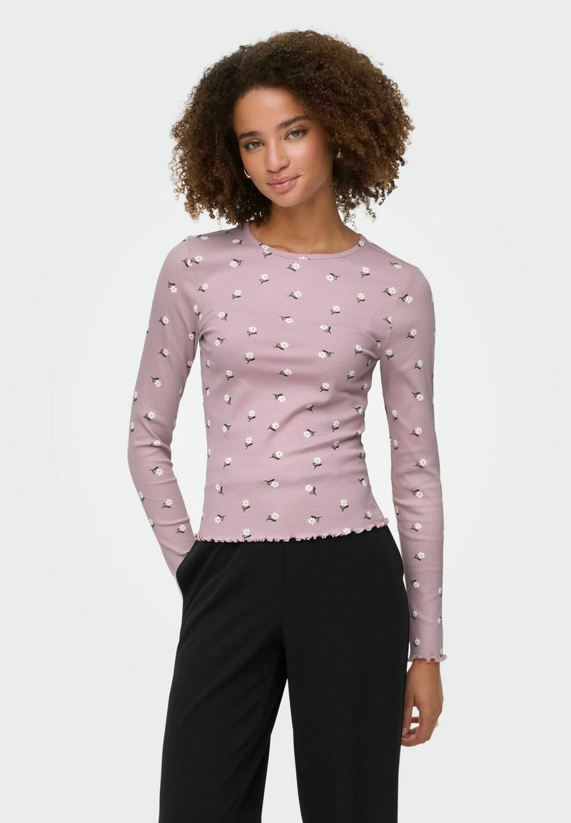 Różowa bluzka z długim rękawem w prążki z białym kwiatowym wzorem, z okrągłym dekoltem i falbanką na dole, zestawiona z czarnymi spodniami.