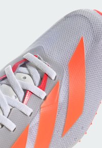 Szare buty sportowe z białymi sznurówkami, z jasnopomarańczowymi akcentami i fakturowanym wierzchem. Zaprojektowane z myślą o wydajności, mają smukły kształt.