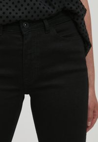 Fekete farmernadrág, slim fit fazonnal, klasszikus öt zsebes kivitelben, övhurkokkal és felső gombos záródással. Sima felület.