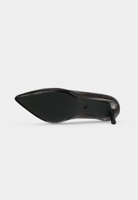 Semelle noire à bout pointu avec petit talon d'une chaussure à talons hauts imprimée léopard marron foncé sur fond blanc.