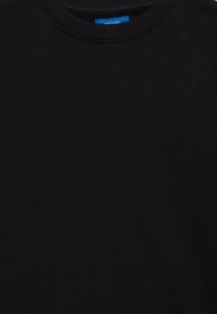 Sweatshirt negru cu guler rotund, confecționat dintr-un material moale, având un guler ribat și un mic eticheta albastră cu textul "REDEFINED" la guler.