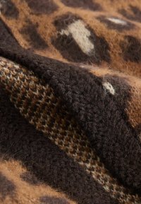 Rjav in črn pleteni material z teksturiranimi vzorci in različnimi debelinami niti, ki ustvarjajo zložen, prijeten površin.