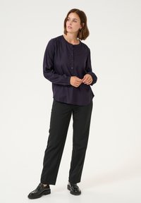 Blouse bleu marine à boutons avec des manches longues, détails froncés aux épaules, associée à un pantalon noir droit et des chaussures noires brillantes.