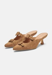 Tacones de ante marrón tipo slingback con punta afilada, pequeño tacón cuadrado y hebillas decorativas en las correas.