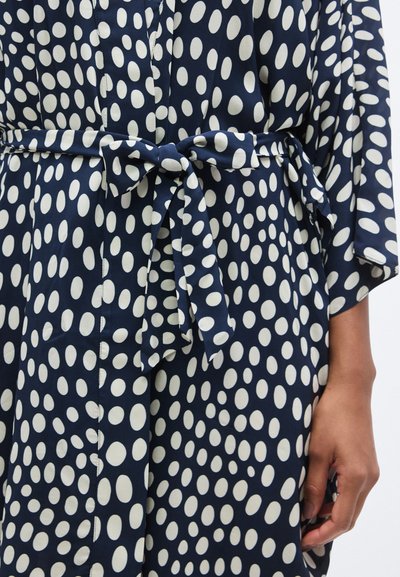 Φόρεμα τύπου wrap από ύφασμα ναυτικού μπλε με λευκές οβάλ βούλες, διαθέτει ζώνη στη μέση και φαρδιές μανσέτες, λεία υφή και κούμπωμα με κουμπιά μπροστά.
