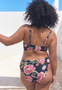 Lilleline bikiini komplekt mustal taustal, millel on roosa pioni ja roheliste lehtede mustrid. Rihmad on reguleeritavad ja topil on kuldne kinnitusdetail.