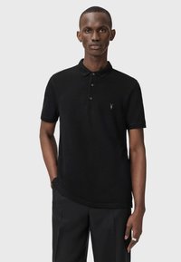 Polo shirt nera con colletto classico, bottone a tre pezzi e logo ricamato sul lato sinistro del petto; tessuto di cotone morbido; maniche corte.
