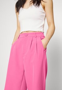 Rosa plisserade byxor med knapp i midjan och fickor, kombinerade med ett vitt kort linne. Mjukt tyg med en slät textur.