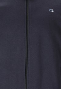 Marineblå zip-up jakke lavet af blødt stof med en sort lynlås og et lille logo i lys blå på venstre brystområde.