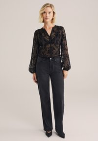 Blusa nera trasparente con ricami floreali, scollatura a V e maniche lunghe, abbinata a jeans neri a vita alta con silhouette dritta.
