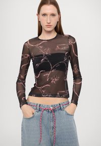 Schwarzes, durchscheinendes Langarmoberteil mit rosa Blumenmustern, figurbetontem Design, rundem Ausschnitt und flachen Nähten. Kombiniert mit hochtaillierten Jean-Shorts.