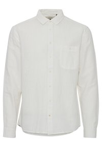Camisa de lino blanca de manga larga con cuello abotonado, bolsillo delantero y una textura sutil. Presenta un dobladillo recto y mangas largas.