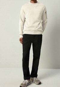 Sudadera gris claro con cuello y puños acanalados, combinada con pantalones negros. Zapatillas deportivas en gris y blanco completan el conjunto.