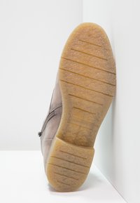 Hnědé semišové kotníkové boty s gumovou podrážkou, která má texturovaný povrch a horizontální drážky, se zipem na boku.