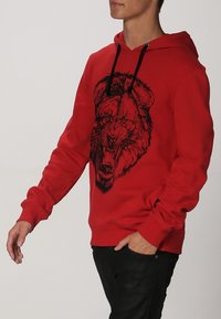 Roter Kapuzenpullover aus Baumwolle mit großem schwarzem Löwenmotiv auf der Vorderseite, ausgestattet mit verstellbarer Kapuze und gerippten Bündchen und Saum.