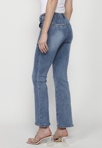 Högmidjade blå denimjeans med rak benpassform, har två bakfickor och lätt blekning, kombinerat med klara klacksandaler.