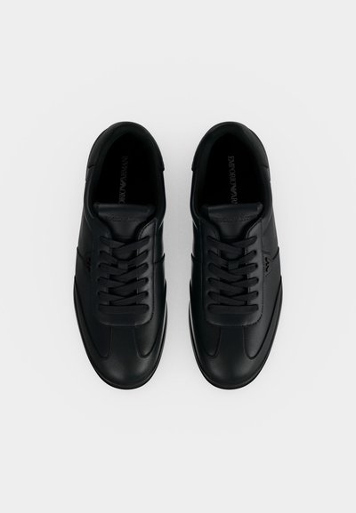 Paire de baskets en cuir noir à lacets, profil bas et marquage discret sur le côté, vues de dessus sur fond blanc.