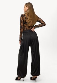 Haut à manches longues en dentelle noire avec motif floral, associé à un pantalon large en satin noir, doté d'une taille haute et d'une coupe ample.