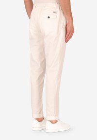 Pantaloni di cotone beige chiaro con vestibilità rilassata, caratterizzati da una tasca posteriore, vita elastica e orli a costine. Indossati con sneakers bianche.