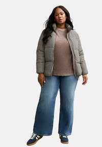 Pufferjack in houndstooth patroon, beige trui, wijdvallende blauwe jeans en marineblauwe sneakers met witte accenten. Vlotte texturen en relaxte pasvorm.