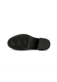 Semelle de chaussure noire avec talon texturé et motif géométrique sur la bande de roulement, présentée à plat sur un fond blanc.