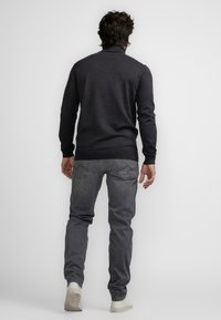 Szary sweter dzianinowy z podniesionym kołnierzem; zestawiony z ciemnoszarymi dżinsami i białymi sneakersami. Miękka tekstura, dopasowany krój, minimalne zdobienia.