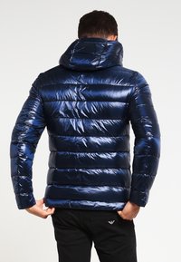 Blå pufferjakke med et skinnende, quiltet design og hætte. Jakken har vandrette striber og elastiske manchetter.