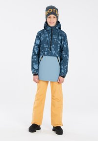 Giacca blu con motivo a fantasia e zip a metà davanti, abbinata a pantaloni impermeabili arancioni e stivali neri. Gli accessori includono un berretto blu con scritte arancioni.