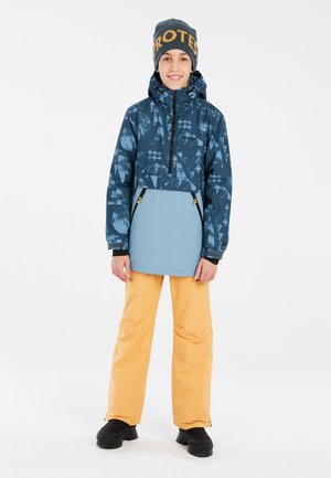 Veste bleue à motifs avec un zip demi-avant, associée à un pantalon imperméable orange et des bottes noires. Les accessoires comprennent un bonnet bleu avec une inscription orange.