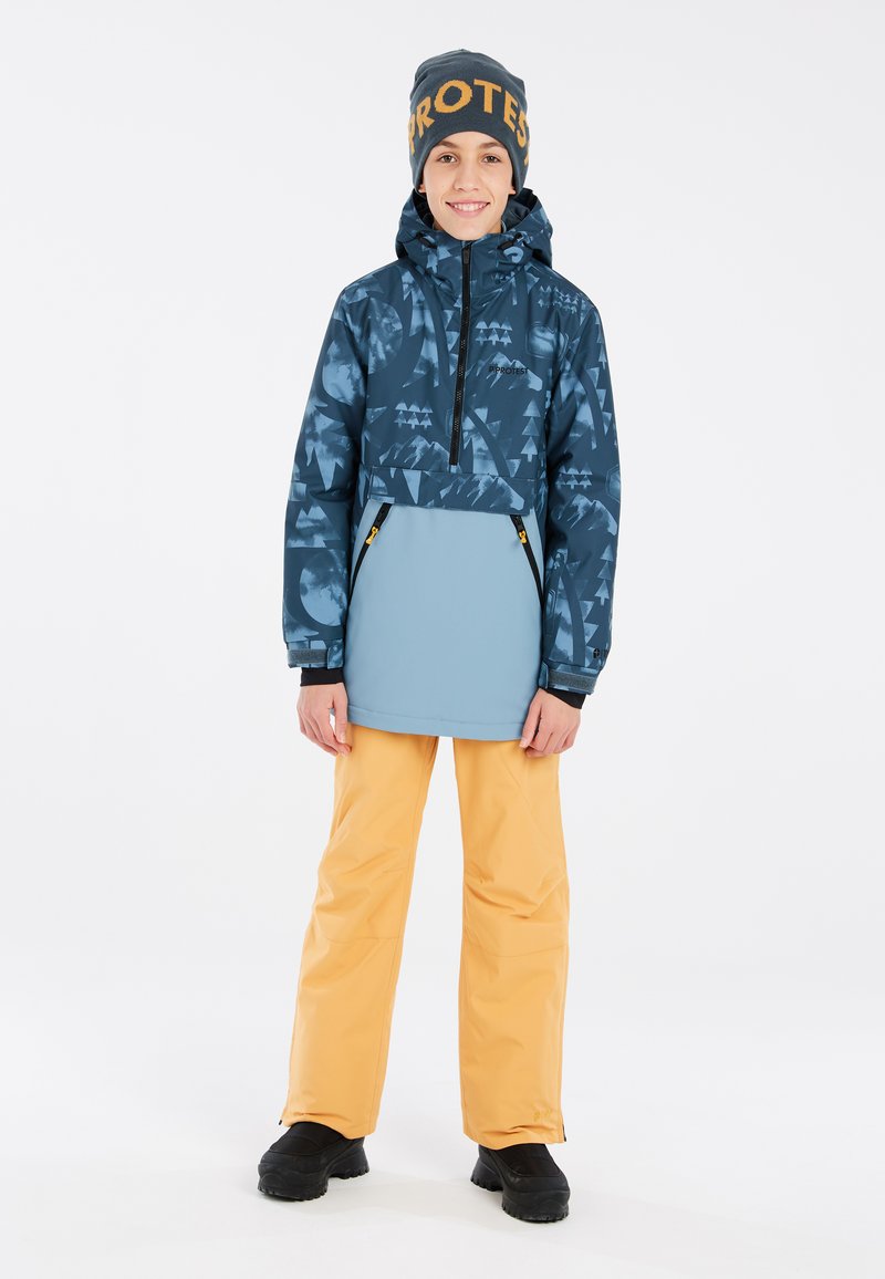 Giacca blu con motivo a fantasia e zip a metà davanti, abbinata a pantaloni impermeabili arancioni e stivali neri. Gli accessori includono un berretto blu con scritte arancioni.