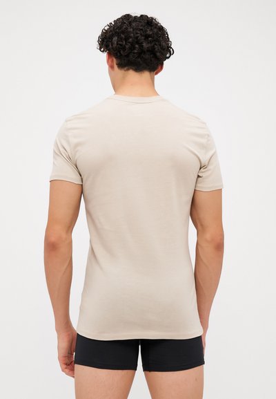 Beige lühikeste varrukatega T-särk, mis on valmistatud pehmest materjalist, klassikalise lõikega ja sileda tekstuuriga, kantud mustade lühikeste pükstega.