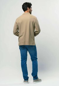 Bež pikk-sleeve särk peene tekstuuriga, koos siniste teksade ja hallide spordijalatsitega. Vaade tagant.