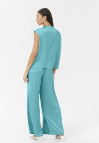 Un ensemble turquoise en deux pièces composé d'un haut sans manches et d'un pantalon large avec des fentes sur les côtés, en tissu texturé et avec une fermeture au dos.