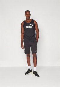 Μαύρη αμάνικη μπλούζα με λευκό λογότυπο "PUMA", συνδυασμένη με μαύρες βερμούδες. Λευκές κάλτσες μέχρι τον αστράγαλο και μαύρα αθλητικά παπούτσια με πράσινες λεπτομέρειες.