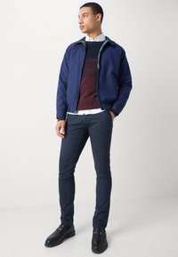 Chaqueta de bombardero azul marino, suéter texturizado burdeos, camisa blanca con cuello, pantalones azul marino ajustados y mocasines negros con acentos de hardware dorado.