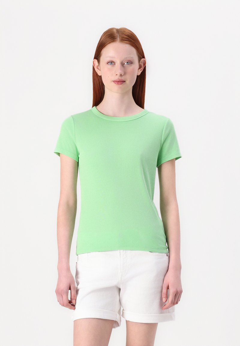 Lysegrøn ribbet bomulds t-shirt med korte ærmer og rund hals, parret med hvide, opsmøgede shorts. Enkel design uden mønstre.