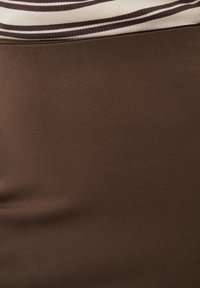 Gros plan d'un tissu marron avec une couture courbée près du haut et une petite section de tissu côtelé beige et marron rayé au-dessus.